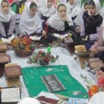 دانش‌آموزان دختر حول میزی پر از گل و تزئینات در حال شرکت در مراسمی مدرسه‌ای