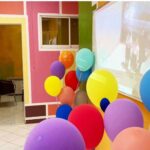 فضای داخلی مدرسه با دیوارهای رنگین و تزیینات بالون‌های رنگی متعدد برای یک فعالیت یا رویداد دانش‌آموزی