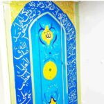نقاشی دیواری با طراحی قوسی، نوشتار عربی و نمادهای زرد روی پس‌زمینه آبی در داخل ساختمان مدرسه
