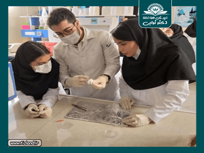 دانش‌آموزان و معلم در حال آزمایش و بررسی یک نمونه فسیل‌شناسی‌ای در آزمایشگاه با تجهیزات حفاظتی