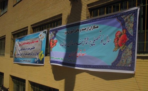 نمای بیرونی ساختمان مدرسه با درب و پنجره‌های فلزی و بنرهای دیواری موقت