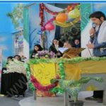 مراسم رسمی تجلیل در مدرسه با تزیینات گلی و بنرهای رنگی، حضور مسئولان و کارکنان
