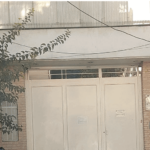 درب ورودی ساختمان آجری‌سازی شده با گیاهان سبز و سقف شیبدار