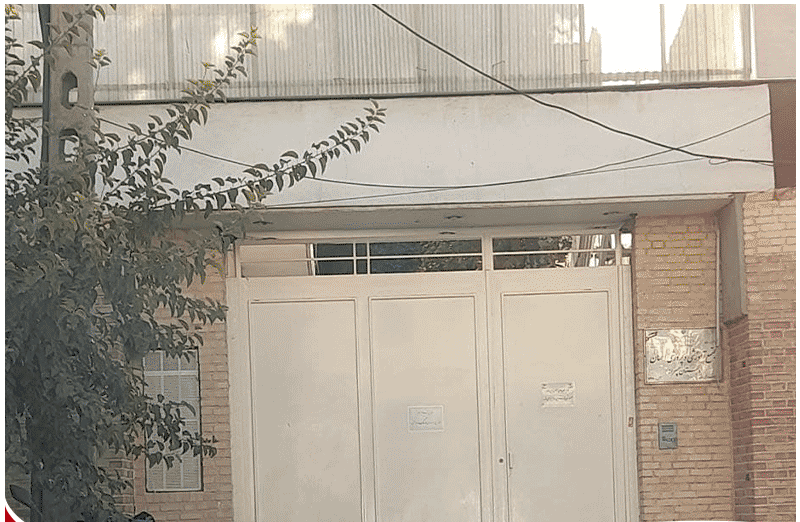 درب ورودی ساختمان آجری‌سازی شده با گیاهان سبز و سقف شیبدار