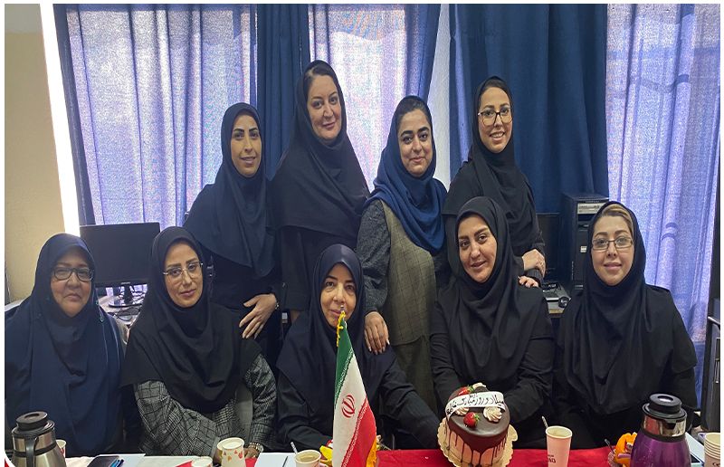 گروهی از زنان در یک جلسه رسمی دور میز با پرچمِ ایران