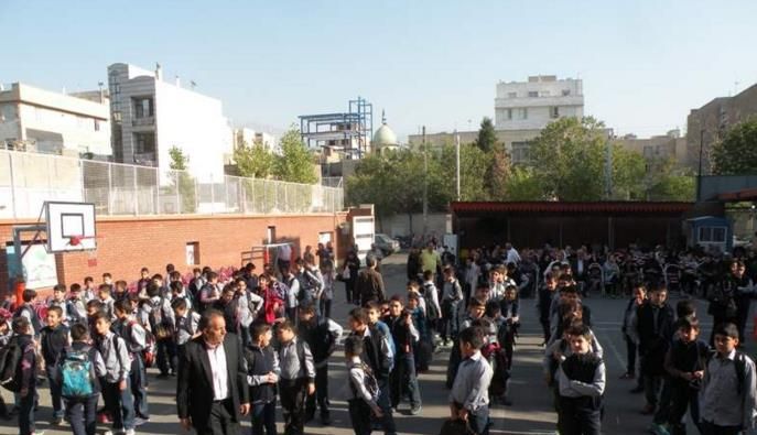 تجمع صدها دانش‌آموز در حیاط مدرسه؛ مراسمی یا جمع‌آوری جمهوری با حضور جمعی از شاگردان در ردیف‌های منظمی در کنار تاسیسات ورزشی (سبد بسکتبال) و دیوارهای آجری شهری