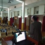 نمای داخلی سالن غذاخوری با صندلی‌های آبی ترتیب‌شده در سفره‌های نقره‌ای، درب‌های قرمز در پس‌زمینه، و یک مسئول در حال تنظیم تکنولوژی