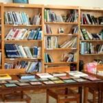 کتابخانه مدرسه با قفسه‌های چوبی پر از کتاب‌های متنوع‌رنگ و میز مطالعه