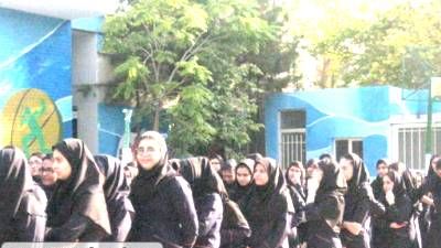 تصویری از تجمع بزرگ دانش‌آموزان دختر در لباس یکدست که در حیاط مدرسه برپا‌شده و یک مراسم یا رویداد جماعی را نشان می‌دهد