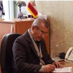 اتاق دفتری یا اتاق مدیریت مدرسه با میز چوبی، پرچم ایران، کتاب‌ها و تلفن دیجیتال