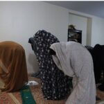 دانش‌آموزان دختر در حال نماز جماعت در نمازخانه مدرسه، ایستاده روی فرش نماز