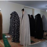 نمازخانه مدرسه‌ای با افراد در حال نماز و جایزه‌های سبز نماز روی فرش‌های رنگی