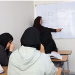 معلمی در حال تدریس درس ریاضی با استفاده از تخته سفید، دانش‌آموزانی در کلاس درس نشسته و درس را دنبال می‌کنند