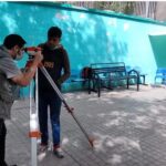 دانش‌آموز در حیاط مدرسه در حال انجام فعالیت اندازه‌گیری و آزمایش علمی تحت راهنمایی معلم