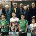 دانش‌آموزان برندگان جام فوتسال در مراسم تجلیل، پوشیده به پیراهن ورزشی سبز و سفید، کنار معاونان و مسئولین مدرسه با جوایز و کاپ
