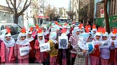 دانش‌آموزانی در لباس رنگین و کلاه‌های رنگی با اوراق در دستان در یک مراسم فرهنگی و هنری