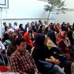 دانش‌آموزان و اساتید در حال شرکت در یک مراسم فرهنگی و هنری داخل سالن مدرسه