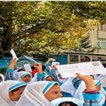 گروهی از دانش‌آموزان با تن‌پوش و کلاه‌های یکسان (آبی و سفید) در حیاط مدرسه در حین یک مراسم یا رویداد جمع‌گی