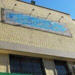 نمای خارجی ساختمان مدرسه فرزانگان با تابلوی دائم آبی رنگ و دیوار آجری زرد