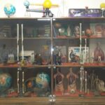 کابینت شیشه‌ای نمایش شامل مدل‌های آموزشی، مدل منظومه شمسی، ماکت‌های معماری، نمونه‌های جغرافیایی و تجهیزات علمی مختلف برای آموزش دانش‌آموزان