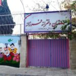 نمای ورودی مدرسه با درب بنفش، تابلوی نام مدرسه و نقاشی دیواری رنگی
