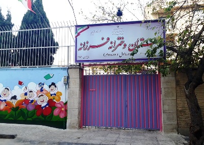 نمای ورودی مدرسه با درب بنفش، تابلوی نام مدرسه و نقاشی دیواری رنگی