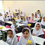 کلاس درسی پر از دانش‌آموزان با روسری سفید در یک مراسم ویژه، هر یک گل زرد در دست می‌گیرند