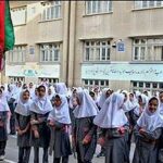 دانش‌آموزان با لباس رسمی درحال شرکت در مراسم رسمی در صحن مدرسه همراه با پرچم ایران