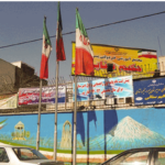 نمای بیرونی سردر و ورودی مدرسه حاکم صنعی با پرچم‌های ملی و تابلوهای اطلاع‌رسانی