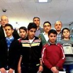 عکس دستهٔ جمعی از معلمان و دانش‌آموزان در اتاق‌ای تزئین‌شده با گل‌های خشک، شمع‌های مختلف رنگ و تابلوهای فارسی روی دیوار