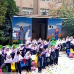دانش‌آموزان مدرسه در حیاط زیر سایبان آبی برای یک رویداد یا مراسم گردهم‌آیی