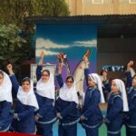 گروهی از دانش‌آموزان دختر با فرم مشخص در حال رفع دست و تشویق در مراسمی در حیاط مدرسه