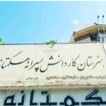 تابلوی نام‌گذاری ساختمان مدرسه هگمتانه به حروف فارسی بر روی دیوار سفید رنگ با آسمان آبی در پس‌زمینه