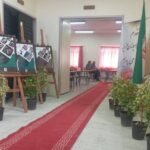 راهرو ورودی ساختمان مدرسه با تابلوهای اطلاعاتی، گیاهان تزیینی و پرچم ایران