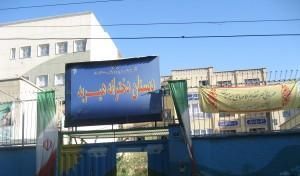 درب و سردر ورودی ساختمان مدرسه با تابلوی نام‌گذاری آبی رنگ و دیوار سفید