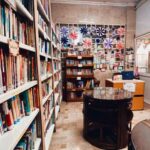 نمای داخلی کتابخانه مدرسه با قفسه‌های کتاب‌های رنگین، میز دایره‌ای مرکزی، و تزئینات دیواری رنگارنگ