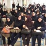 تصویری از گروه بزرگی از دانش‌آموزان دختر با لباس یکدست سیاه، نشسته در کنار هم در یک فضای داخلی، در حین یک رویداد یا جمع‌خوری رسمی مدرسه