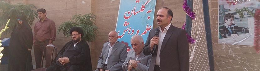 گروهی از مسئولان و مدیران مدرسه در حال سخنرانی و شرکت در یک مراسم رسمی داخل ساختمان با تزئینات و بنرهای فارسی