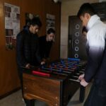 دانش‌آموزان در حال بازی فوسبال (تیکی‌مز) در یک اتاق ورزشی درون مدرسه، تابلوهای آموزشی روی دیوار