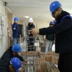 دانش‌آموزانی با کلاه ایمنی در حال انجام یک پروژه ساخت‌وساز و مهندسی عملی درون ساختمان مدرسه