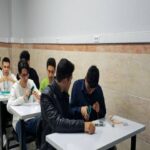 گروهی از دانش‌آموزان در حال انجام فعالیت یا پروژه گروهی در میزهایی در کلاس درس، با تجهیزات و مواد آزمایشی روی میزها