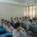 کلاس درسی با دانش‌آموزان پسر نشسته در میزهای آبی، دیوارهای آجری سفید، پنجره‌های بزرگ و روشنایی طبیعی خوب