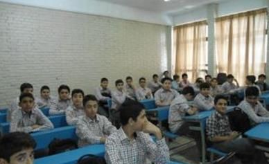 کلاس درسی با دانش‌آموزان پسر نشسته در میزهای آبی، دیوارهای آجری سفید، پنجره‌های بزرگ و روشنایی طبیعی خوب