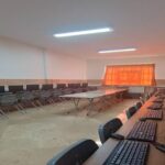 اتاق سایت کامپیوتر مدرسه با میزهای منظم، صندلی‌های سیاه، کیبورد‌ها و مانیتورهای آموزشی