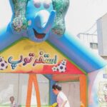 سازه بادی رنگی برای بازی کودکان در حیاط مدرسه، با طرح‌های فوتبال و متن فارسی