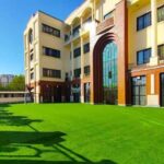 نمایی از حیاط مدرسه با چمن سبز پهناور و ساختمان‌های چند طبقه با معماری رنگین در اطراف