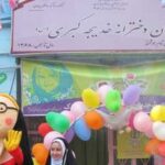 تصویری از یک مراسم جشن و کارنوال مدرسه‌ای با بنر فارسی و گلبالو‌های رنگی و تزیینات جشن
