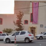 نمای بیرونی ساختمان مدرسه خاجه‌نصیر‌الدین توسی با دیوار صورتی، پنجره‌های قرمز و درب‌های زرد، ماشین‌های پارک شده در جلو