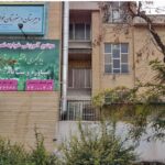 نمای بیرونی ساختمان مدرسه خاجه‌نصیرالدین طوسی با تابلوی دائمی فارسی، درب ورودی، دیوار آجری و درختان دورش