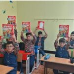 دانش‌آموزان در کلاس درس کتاب‌های قرمز را بالای سر خود نگاه می‌دارند